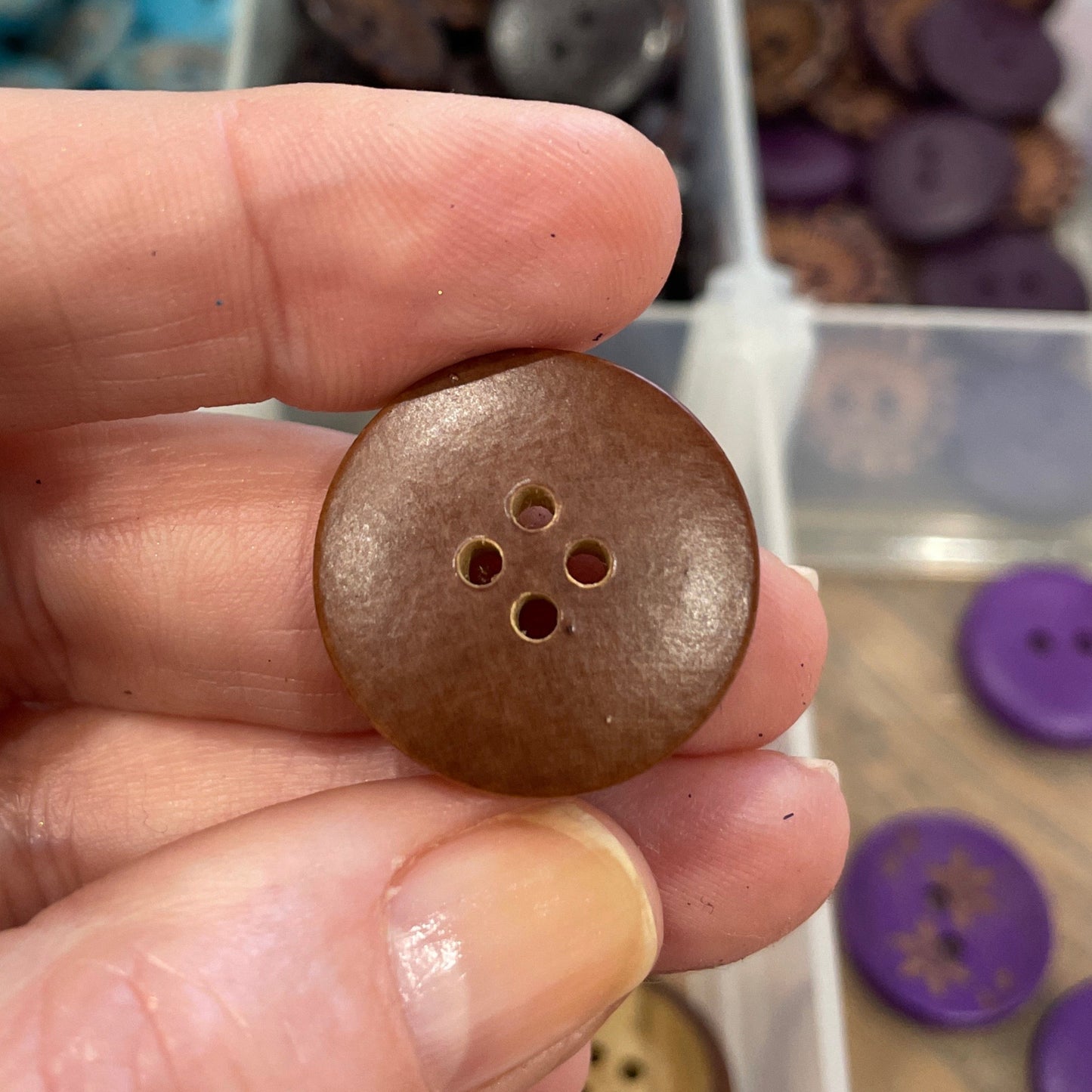 Hand holding a brown button with a clear container of buttons in the background
