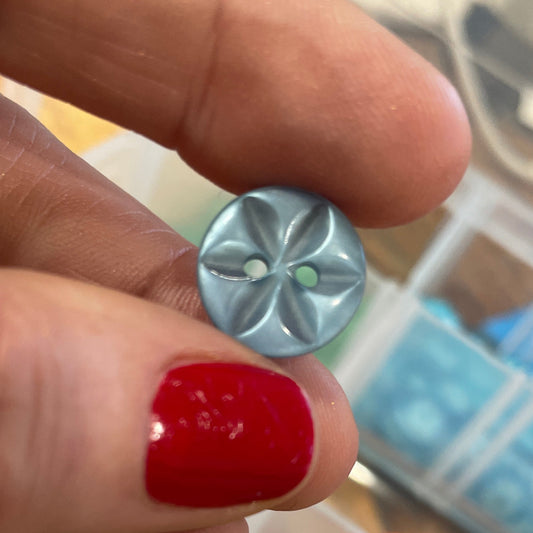 Hand holding a small silver flower-shaped object with a blurred background of colorful items in a box.