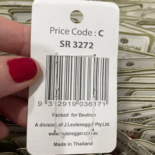 Close-up of a product tag with a barcode and text, held by a hand with red nail polish.