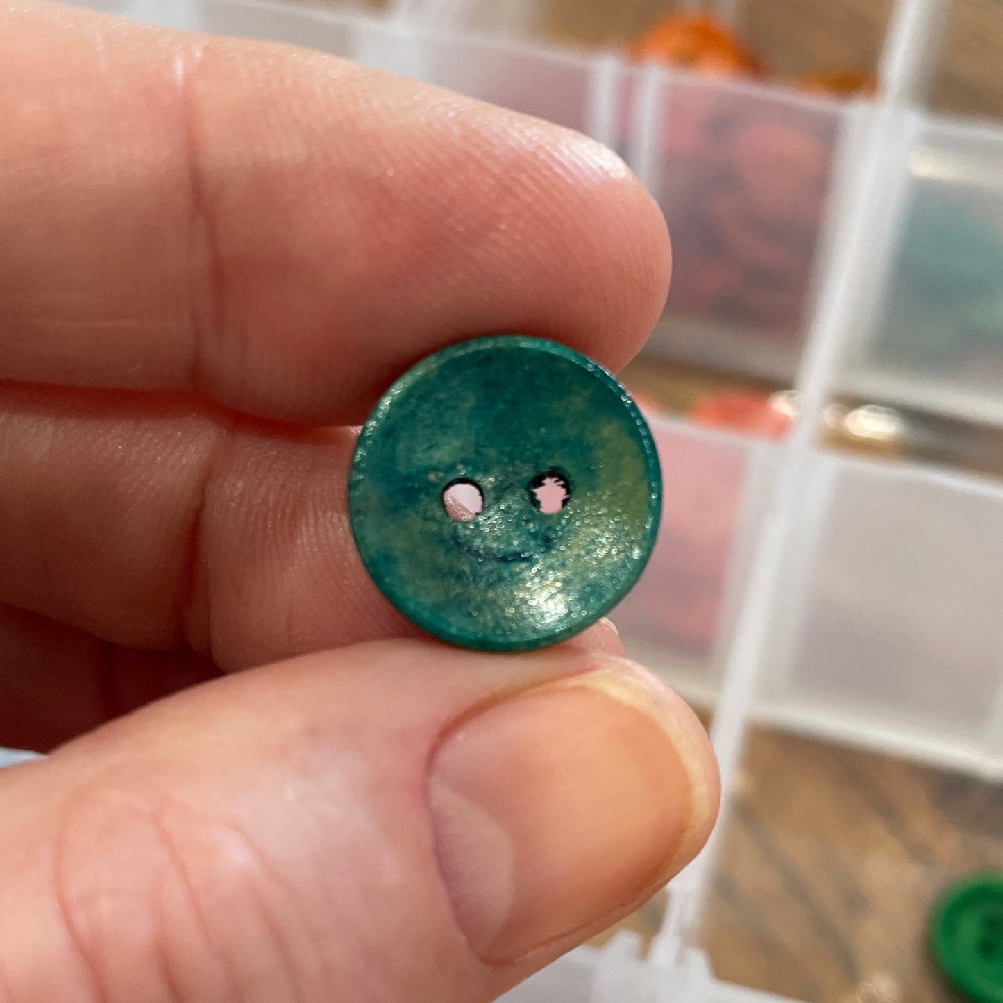 Hand holding a green button with a clear container of buttons in the background