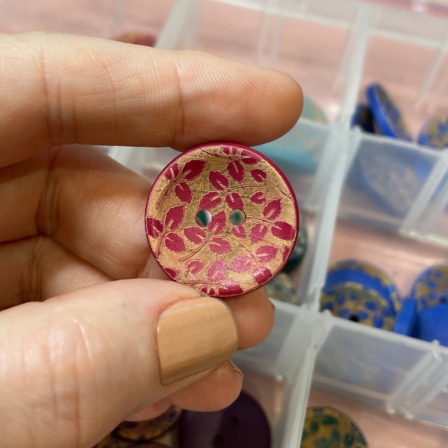 Hand holding a decorative button with a container of other buttons in the background