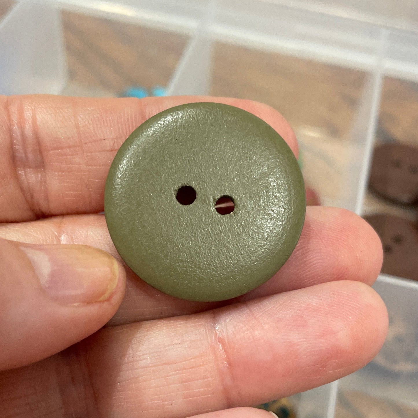 Hand holding a green button with a container of buttons in the background