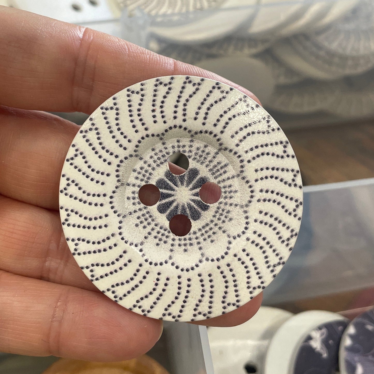 Hand holding a decorative button with intricate design, blurred buttons in the background