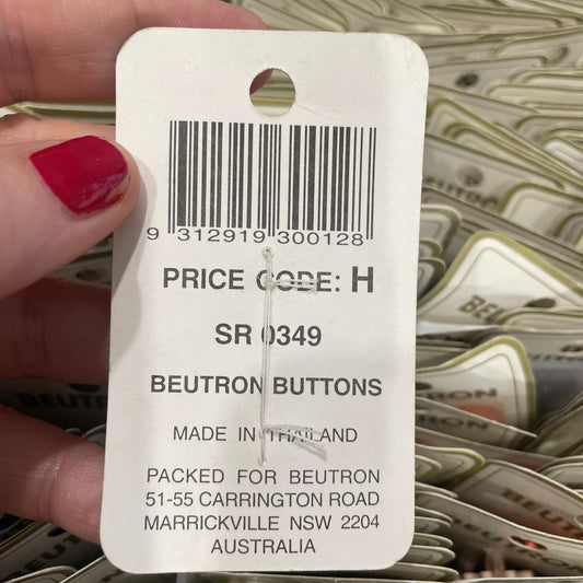 Close-up of a button label held by a hand with red nail polish, showing a barcode and text.