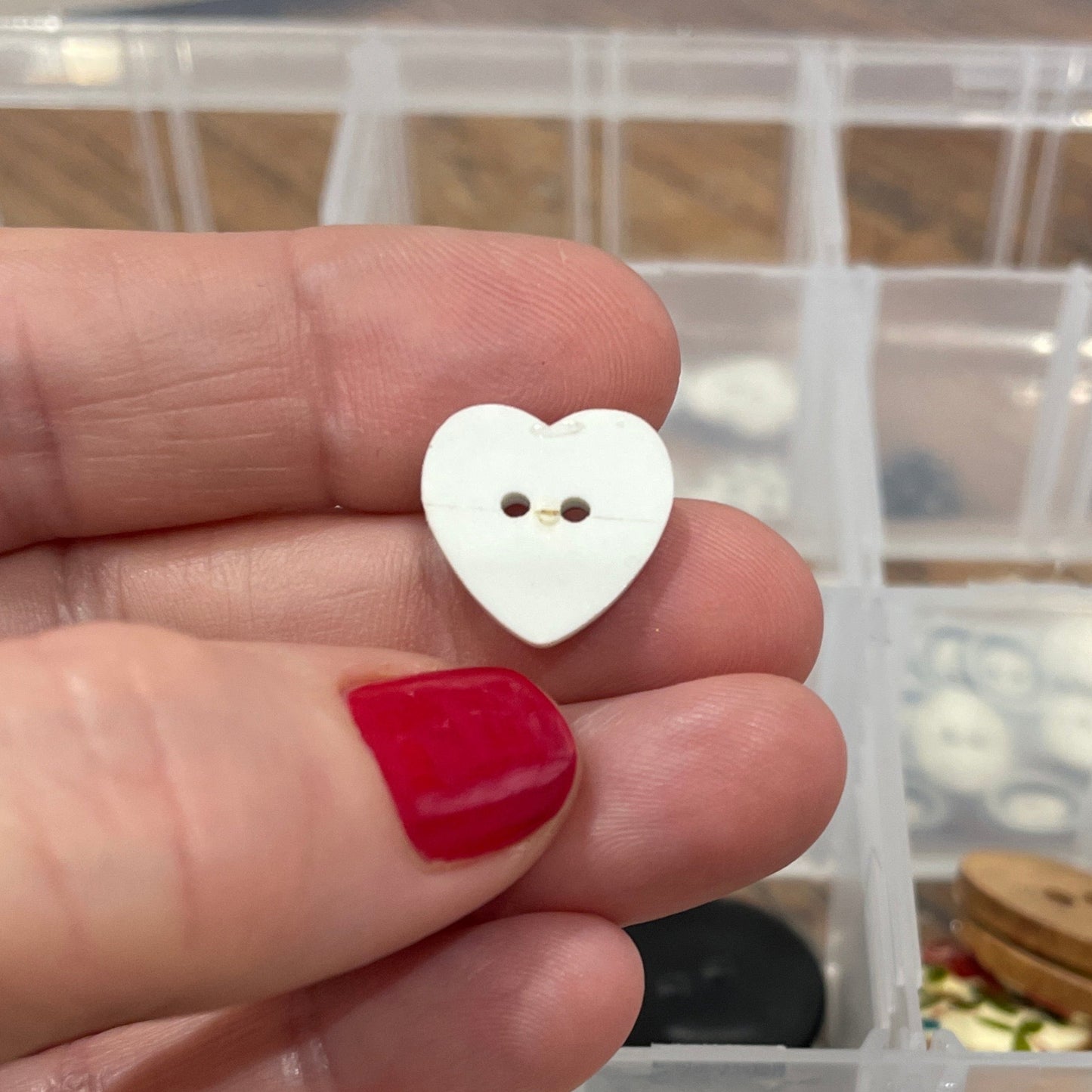Hand holding a white button with a clear container of buttons in the background