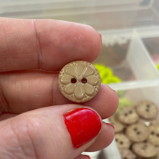 Hand holding a decorative button with a clear container of buttons in the background
