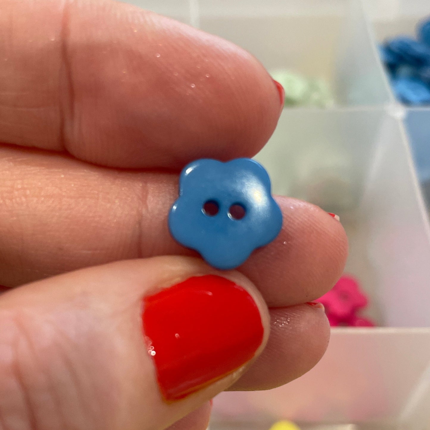 Hand holding a blue button with a background of colorful buttons in a case
