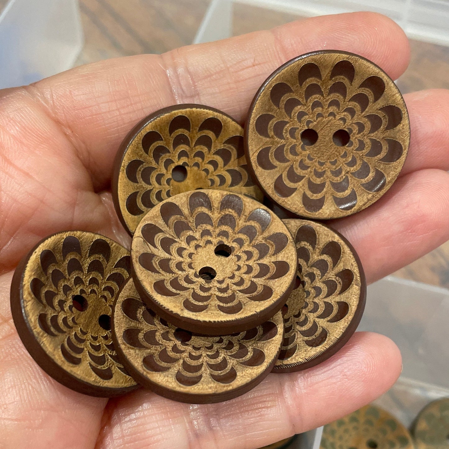 Hand holding decorative wooden buttons with a clear container of more buttons in the background.