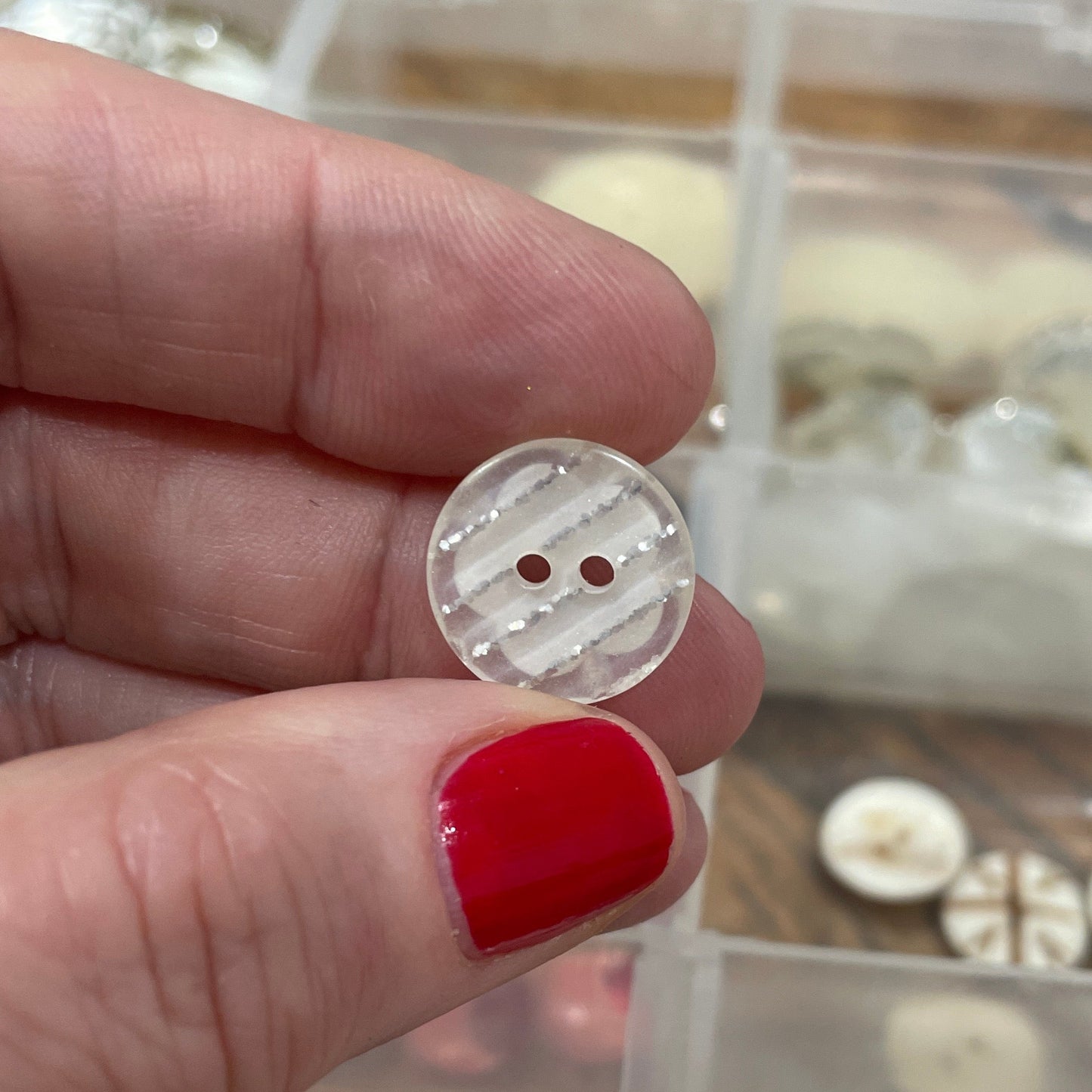 Hand holding a button with a background of button collection in a box