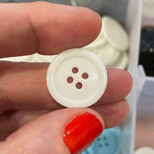 Hand holding a white button with a clear container of buttons in the background