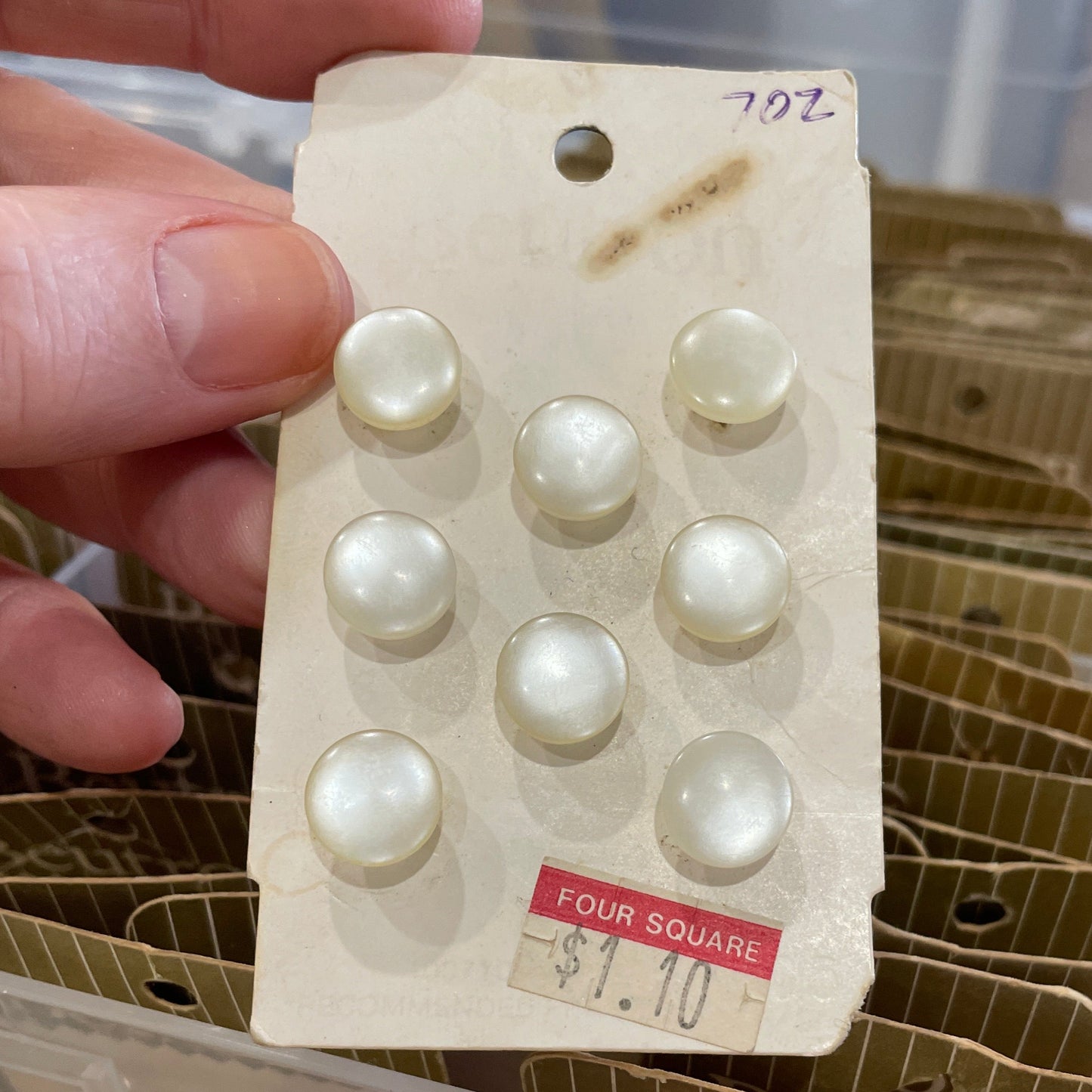 Card with buttons held by a hand, with a container of similar items in the background.
