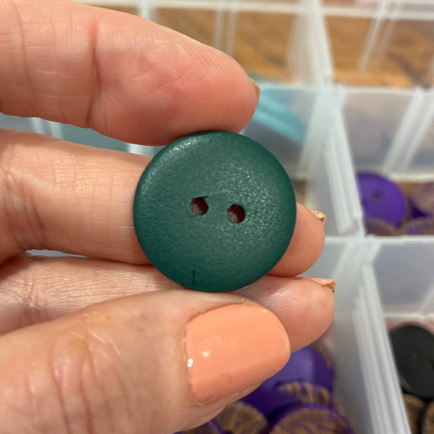 Hand holding a green button with a container of buttons in the background