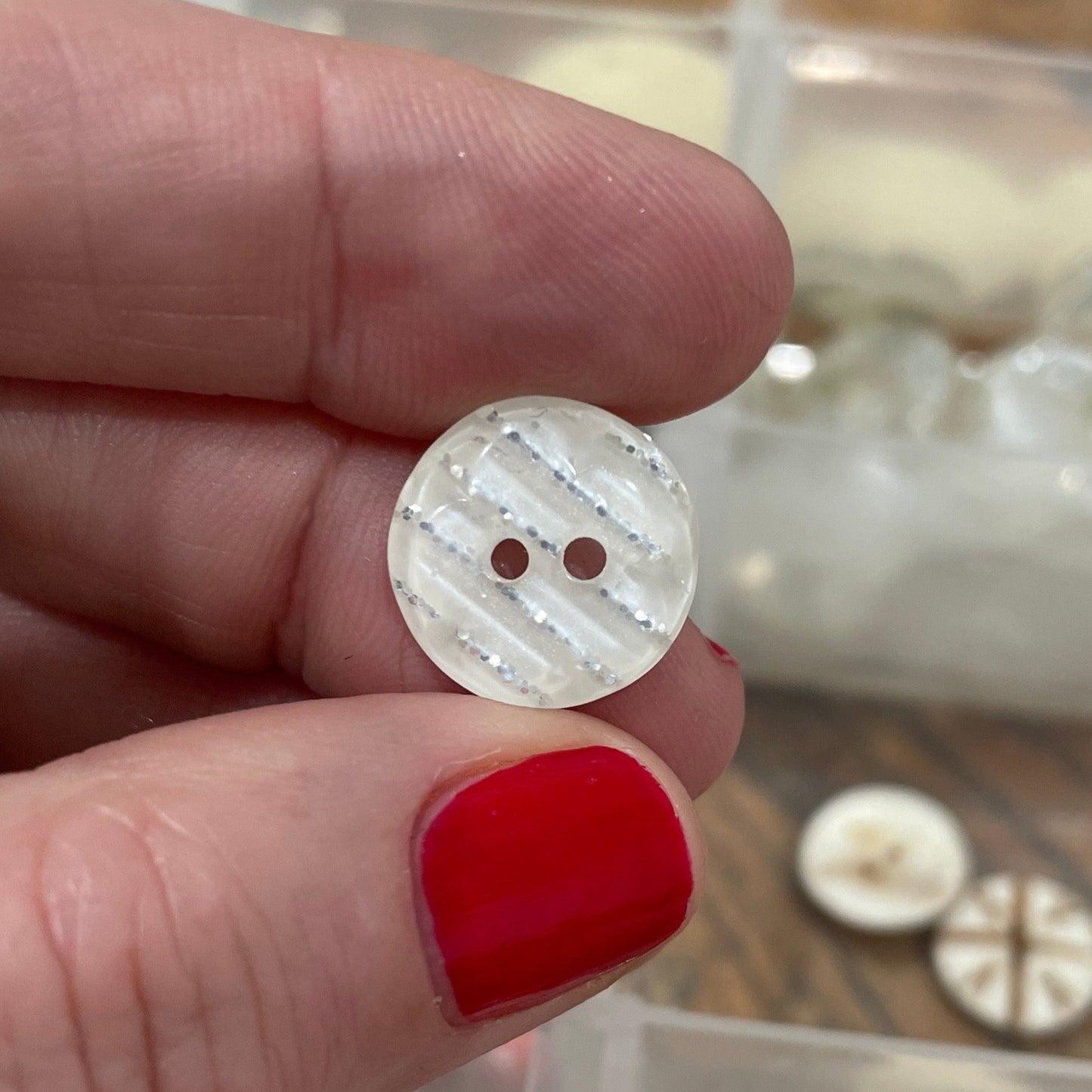 Hand holding a small white button with a clear container of buttons in the background