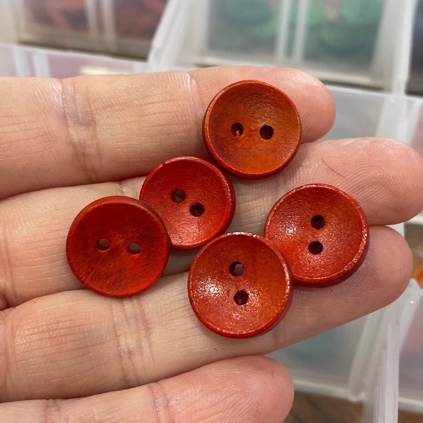 Hand holding red buttons with a container of buttons in the background