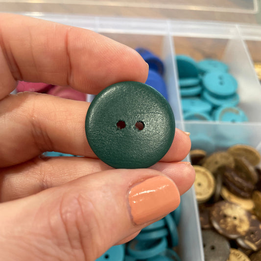 Hand holding a green button with a container of buttons in the background