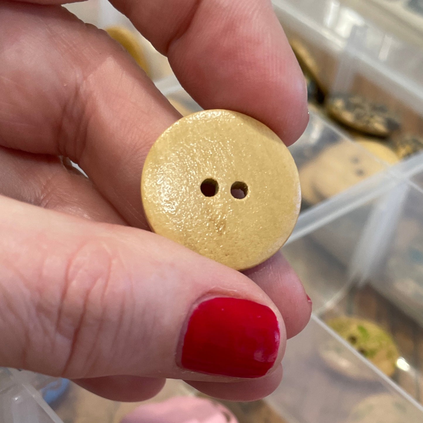 Hand holding a yellow button with a container of various buttons in the background
