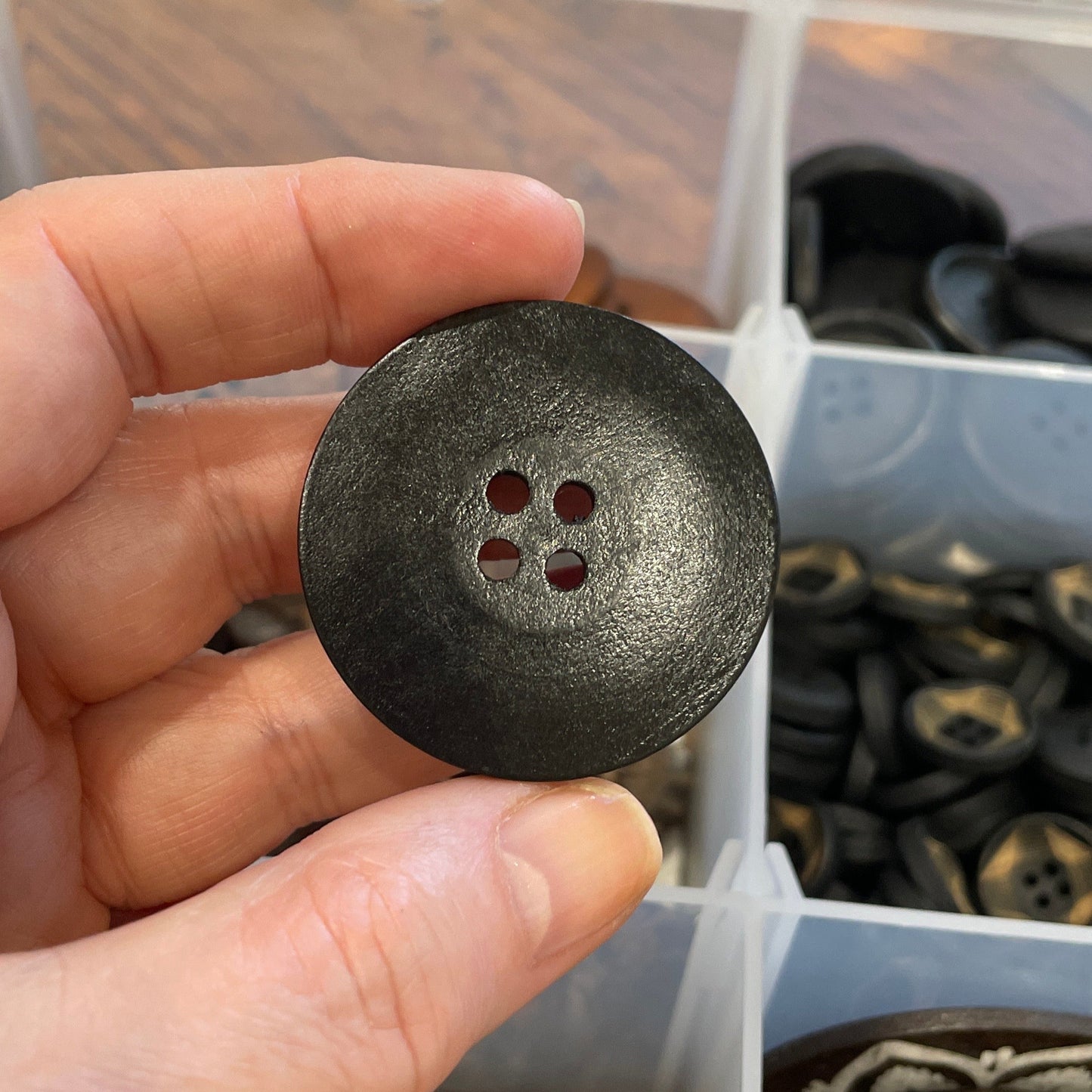 Hand holding a black button over a container of various buttons