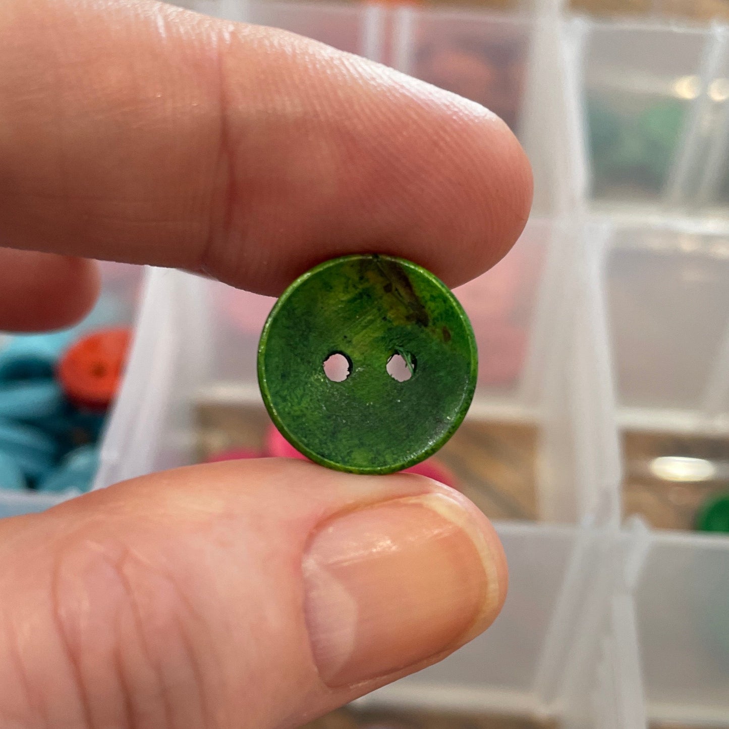 Green button held between fingers with a container of buttons in the background