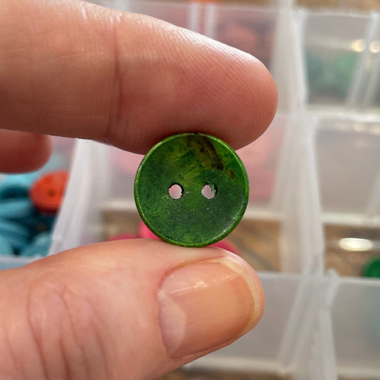 Green button held between fingers with a container of buttons in the background