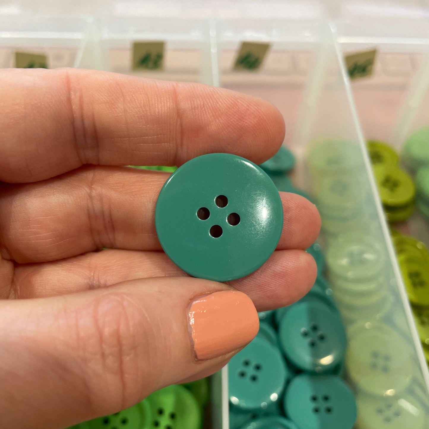 Hand holding a green button with a container of buttons in the background