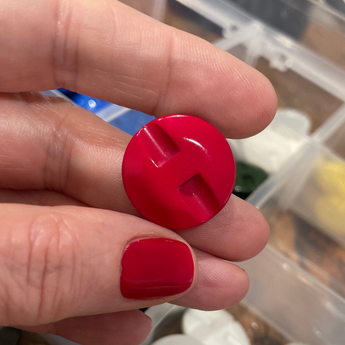 Hand holding a red button with a container of various buttons in the background