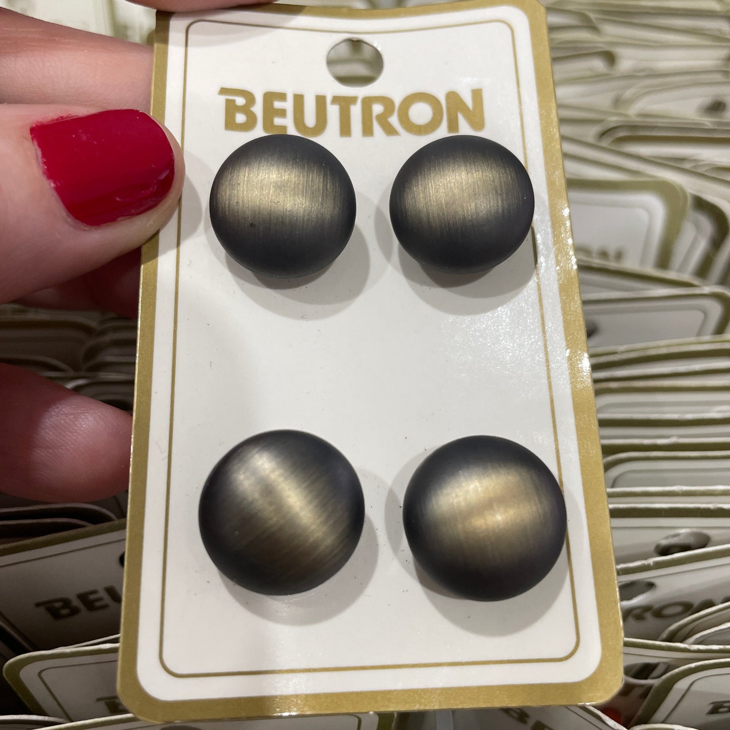 Four buttons on a Beutron branded card held by a hand with red nail polish.
