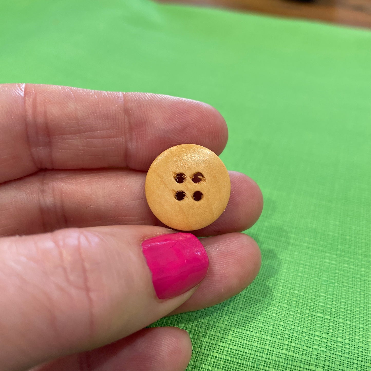 Hand holding a yellow button with four holes against a green background