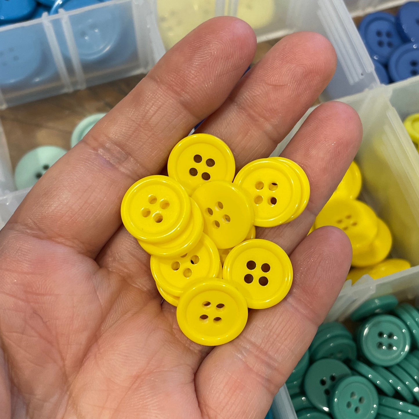 Hand holding yellow buttons with a container of assorted buttons in the background
