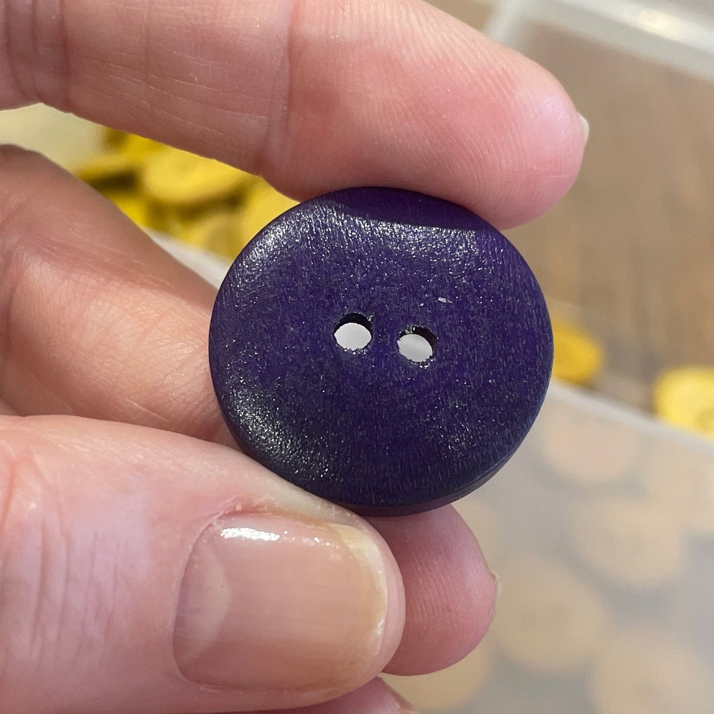 Hand holding a purple button with a clear container of buttons in the background