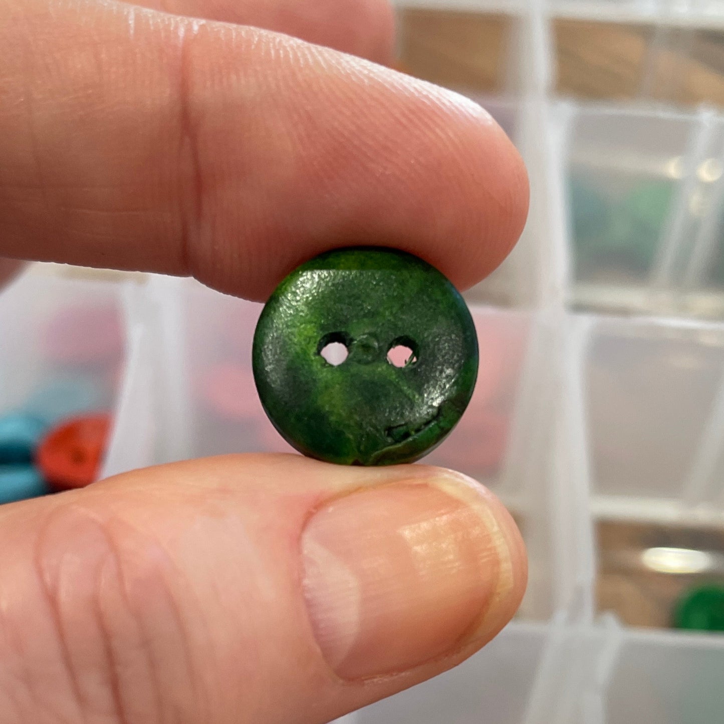 Green button held between fingers with a container of buttons in the background