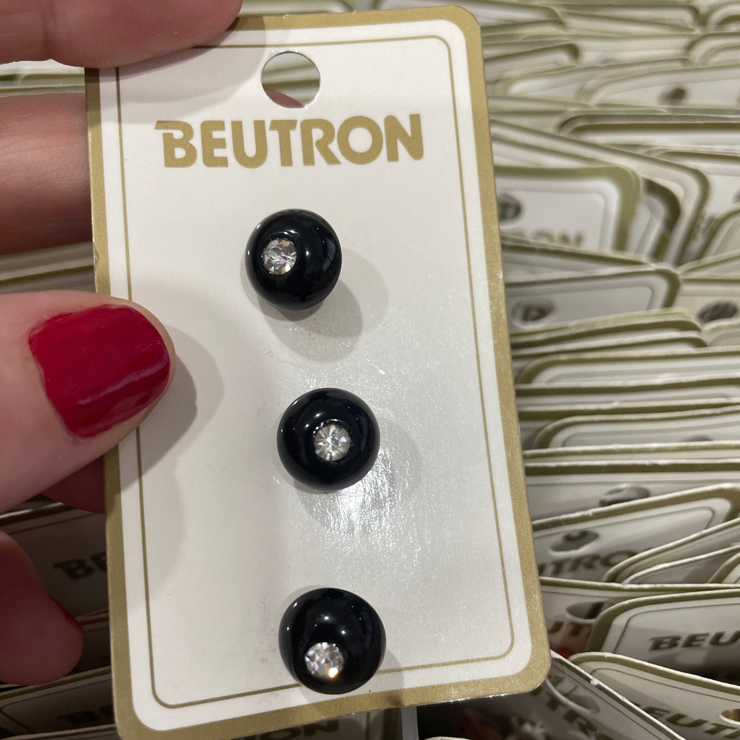 Black buttons on a BEUTRON branded card held by a hand with red nail polish.