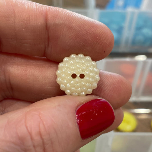 Hand holding a yellow button with a blurred background of a button organizer.