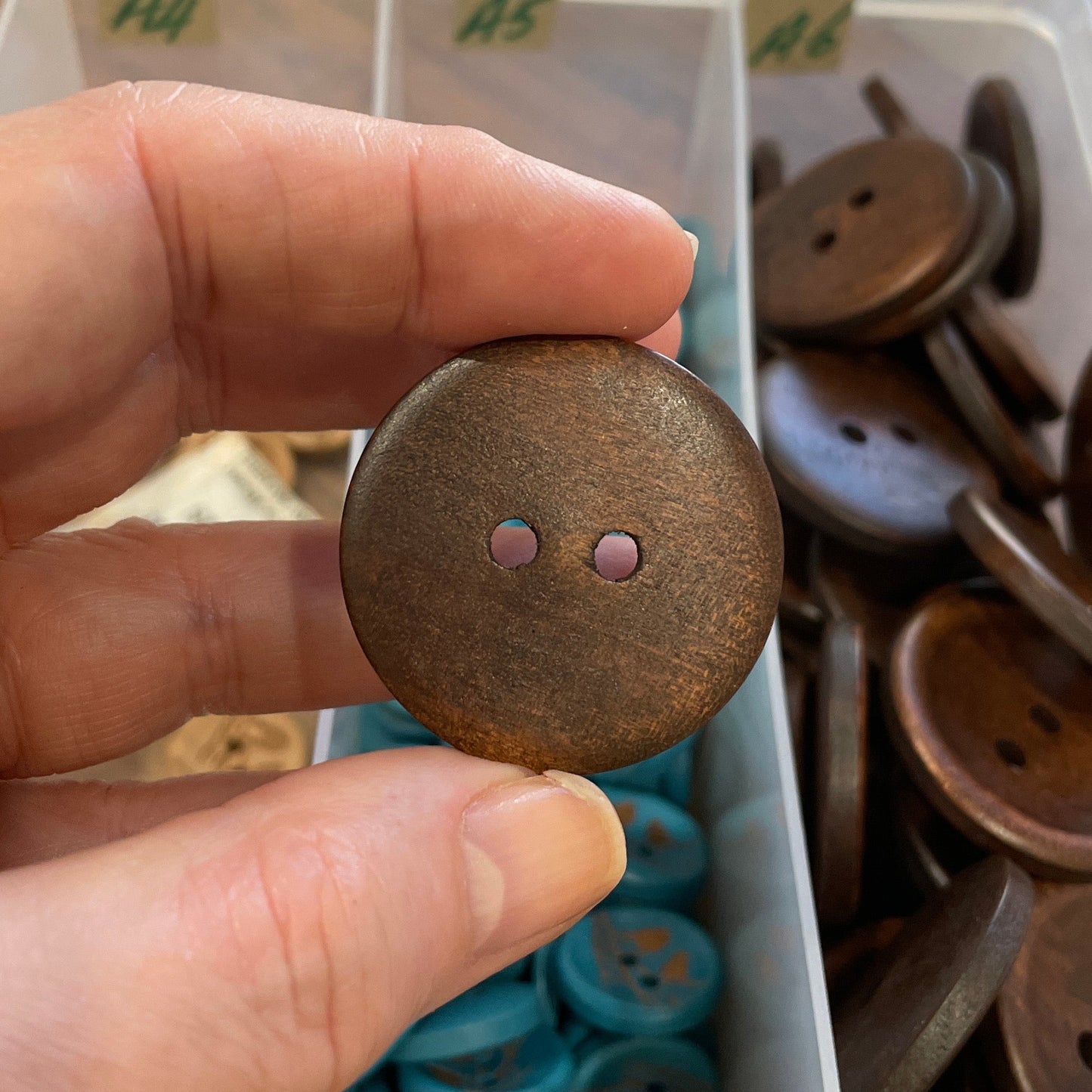 Hand holding a brown button with a container of buttons in the background