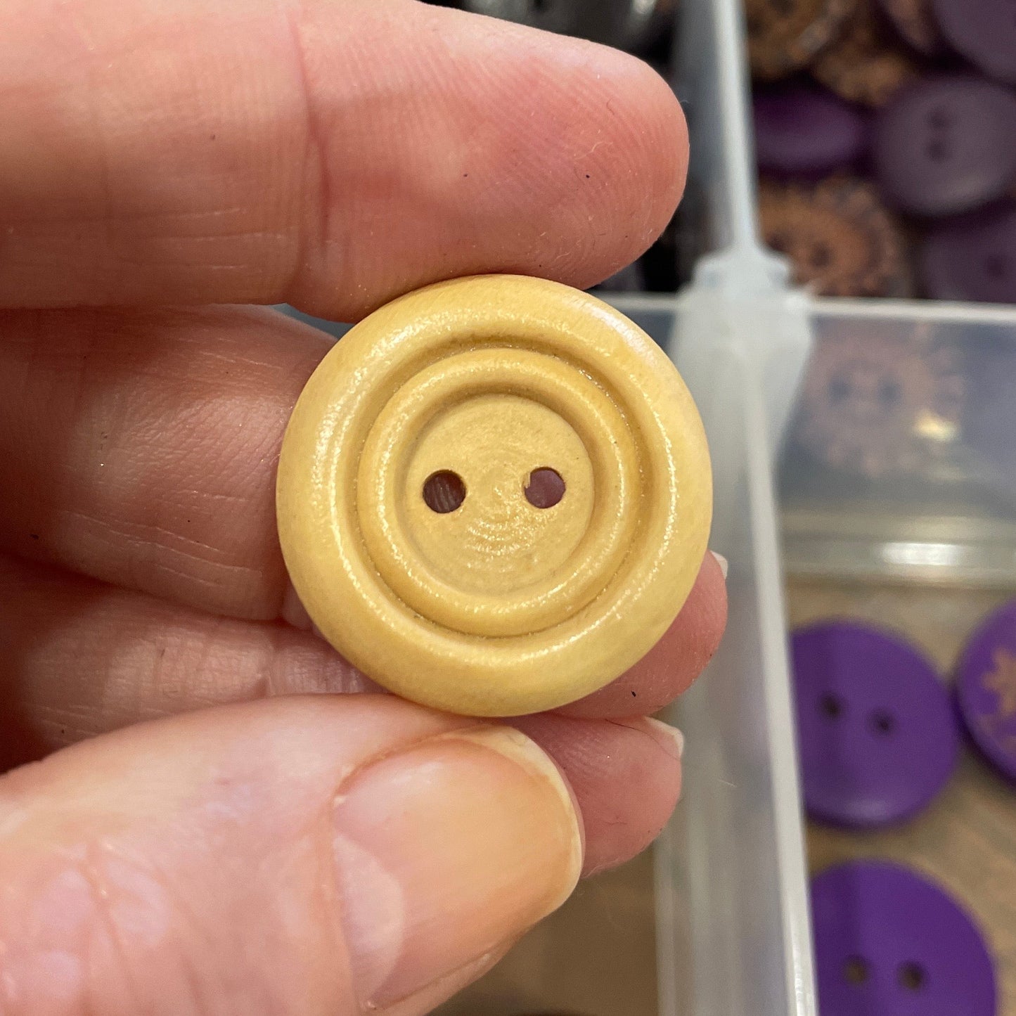 Hand holding a yellow button with a blurred background of button collection