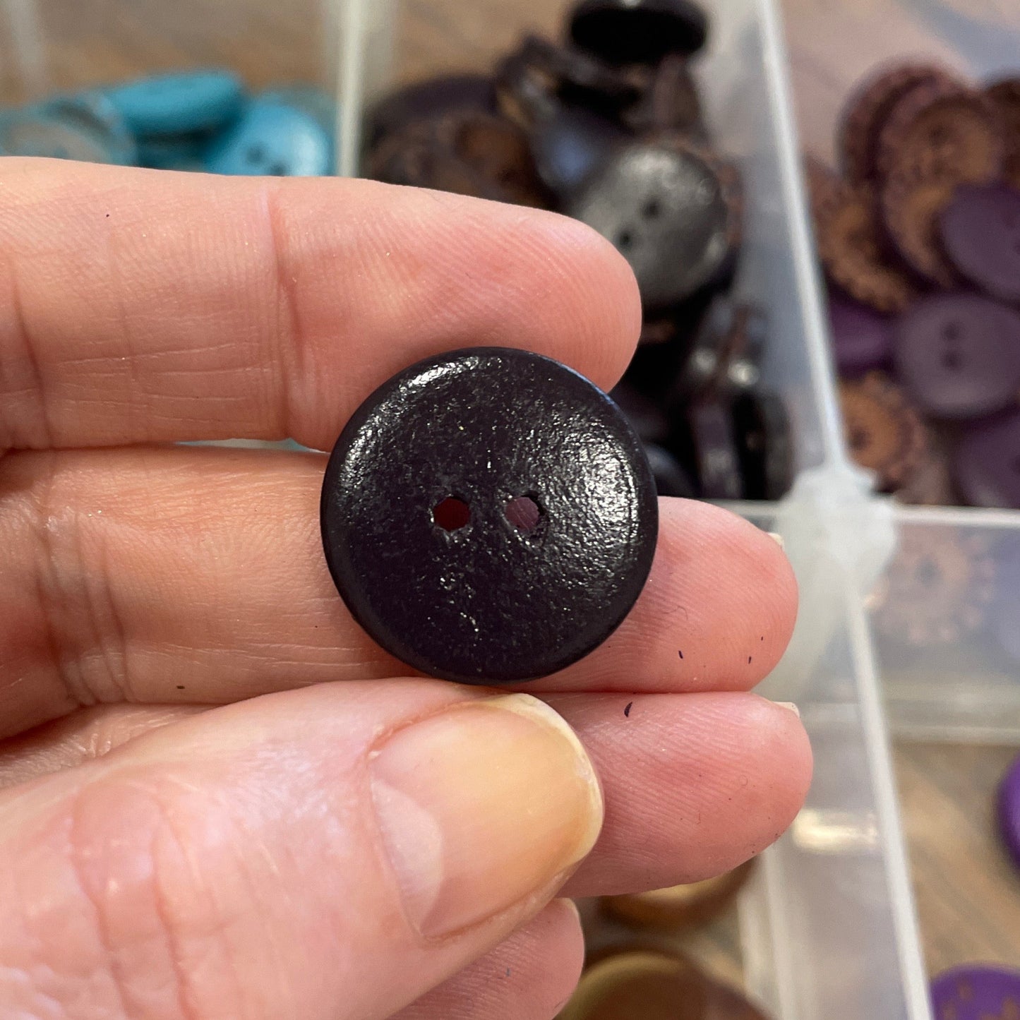 Hand holding a dark brown button with a collection of buttons in the background