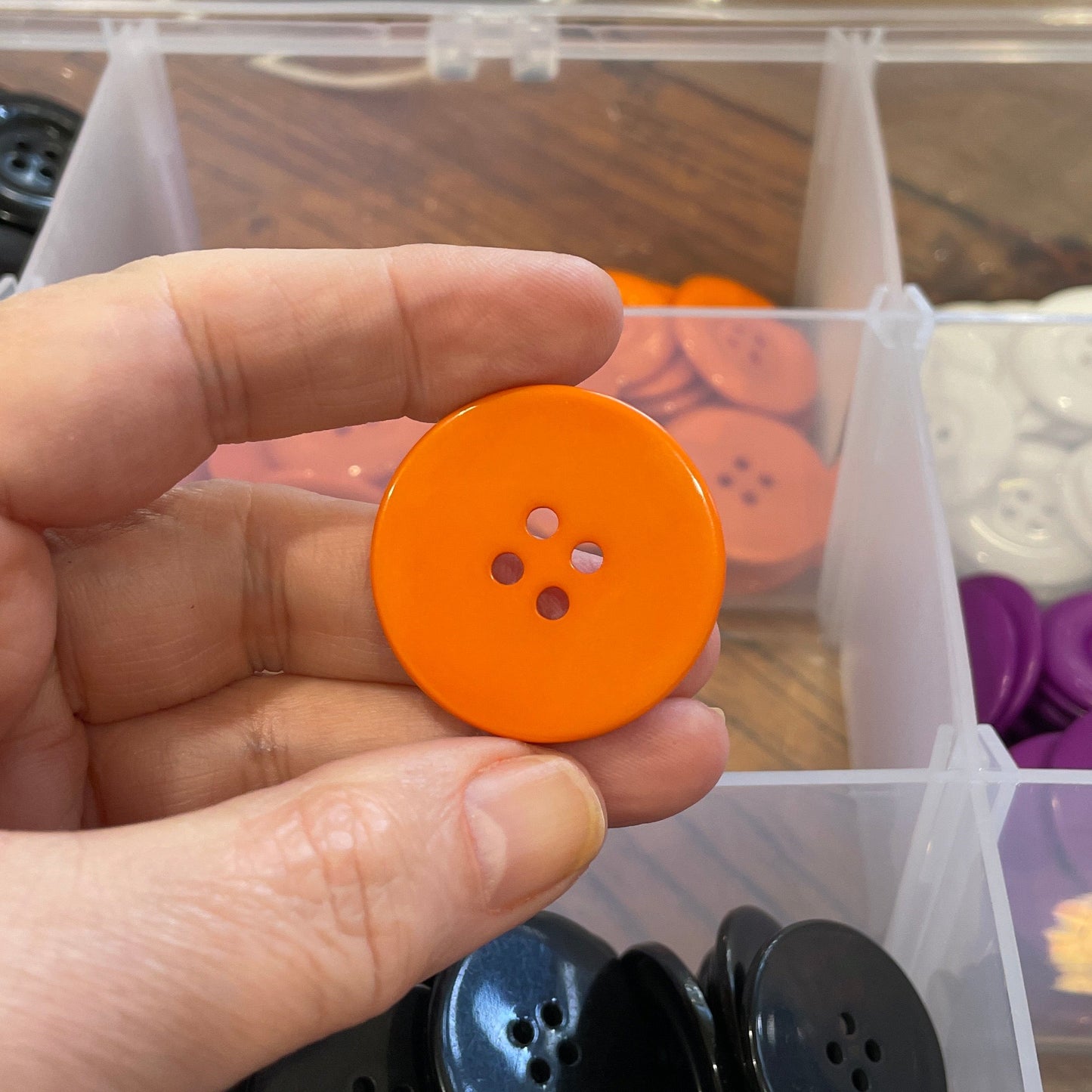 Hand holding an orange button with a container of buttons in the background