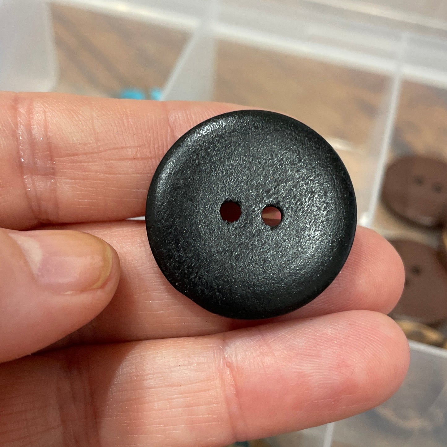 Black button held in a hand with a container of buttons in the background