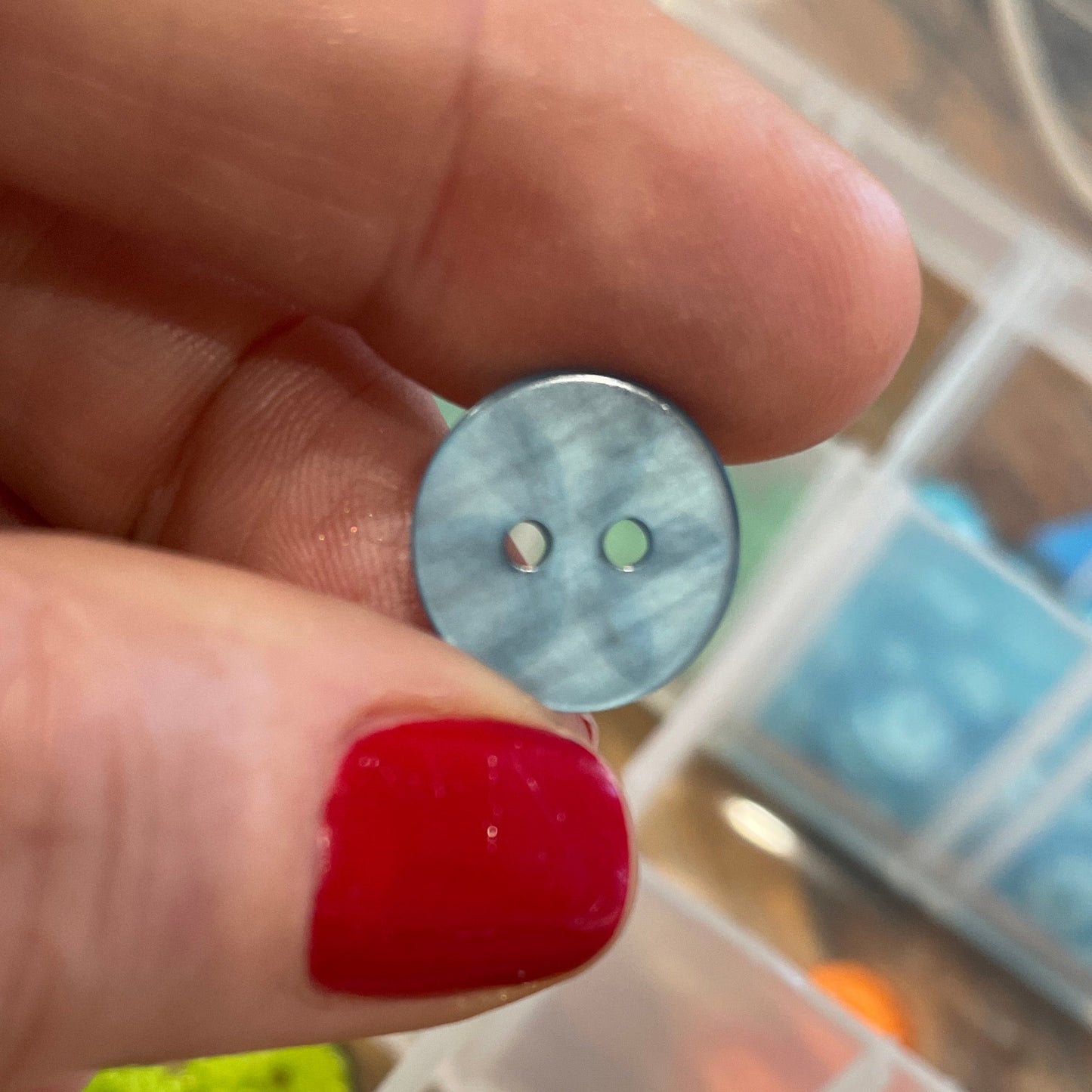 Hand holding a small metal button with a background of colorful buttons in a case.