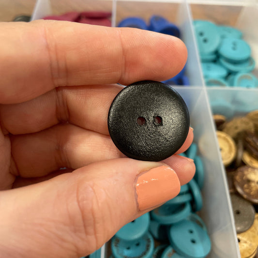 Person holding a black button with a container of buttons in the background
