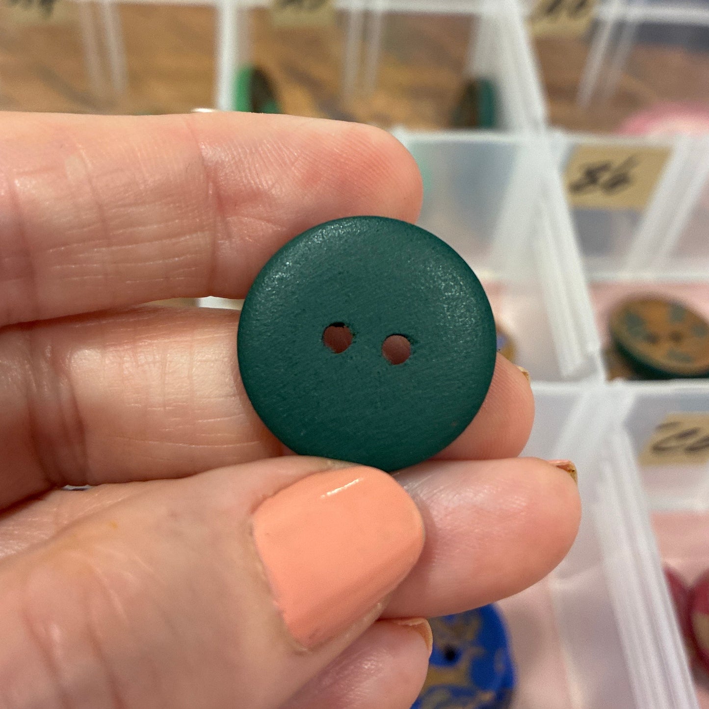 Hand holding a green button with a container of buttons in the background
