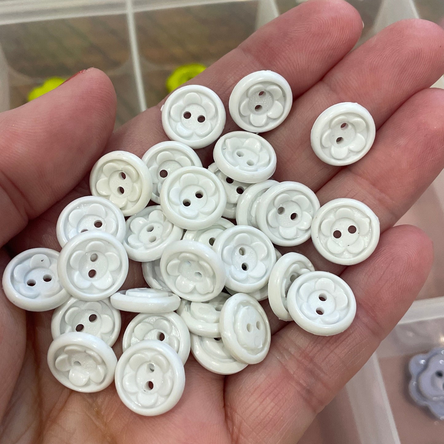 Hand holding white buttons with a container of buttons in the background