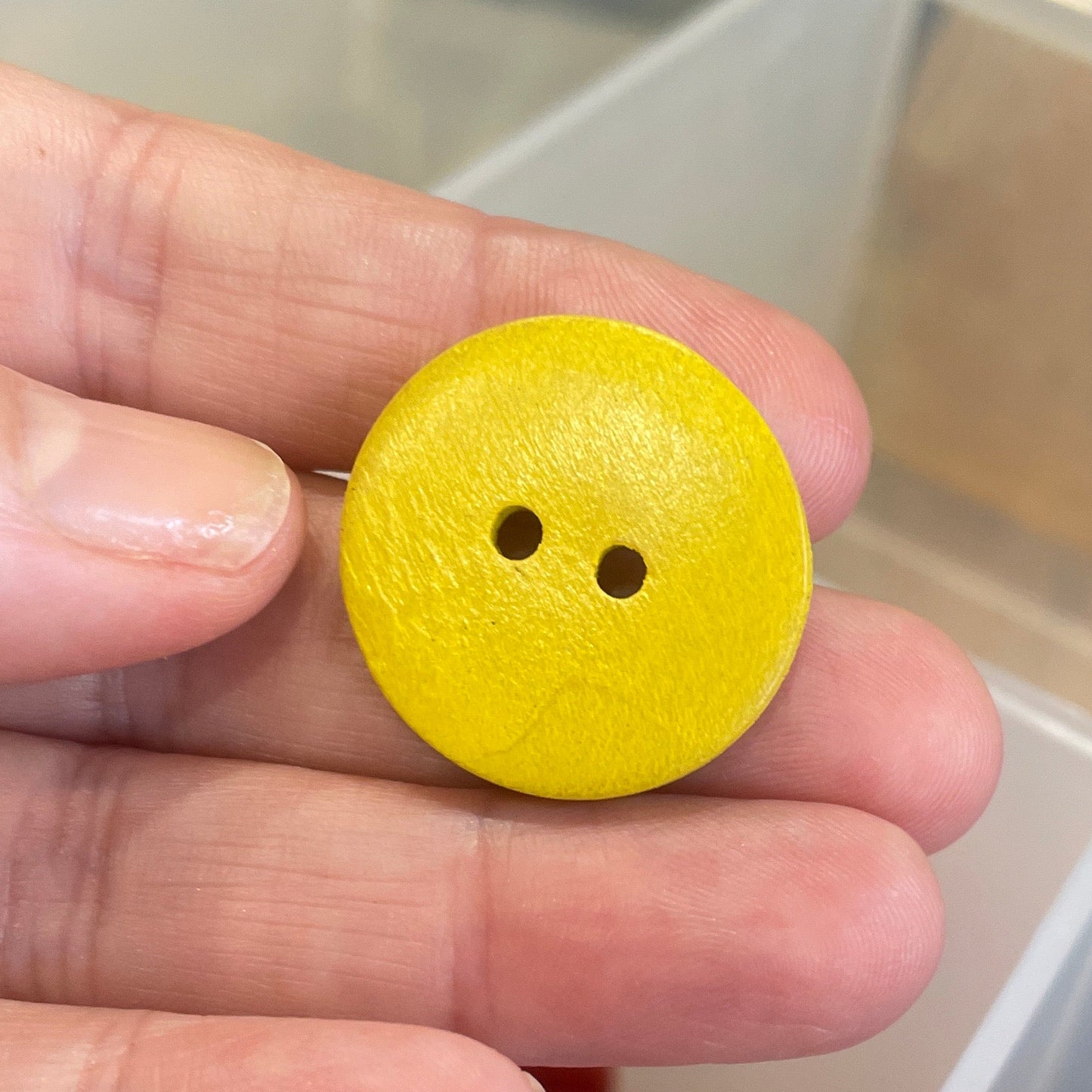 Yellow button held by a hand with a container of buttons in the background