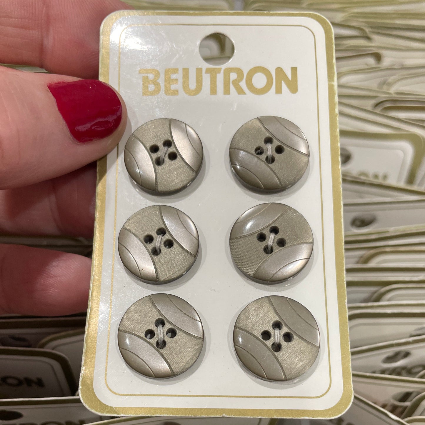Packaging of metallic buttons with 'Beutron' branding held by a hand.