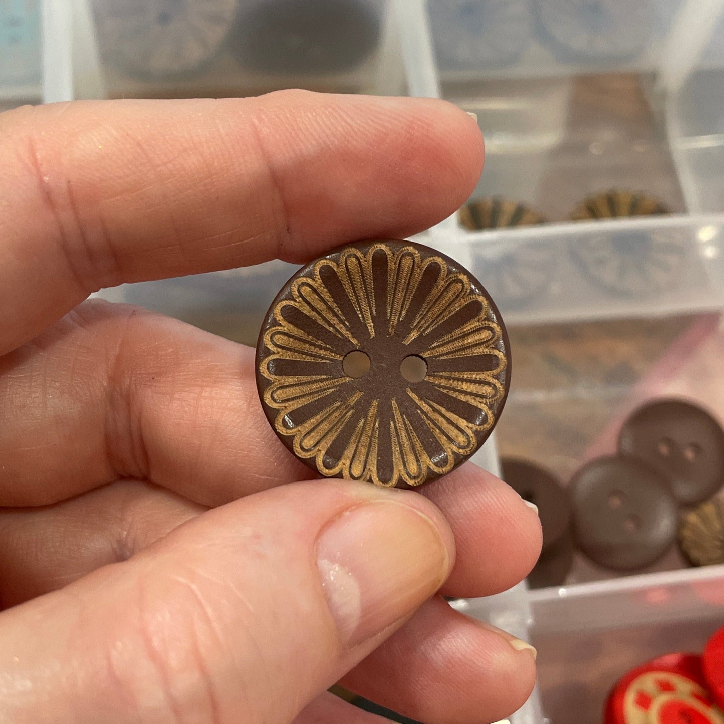 Hand holding a decorative button with a clear container of buttons in the background