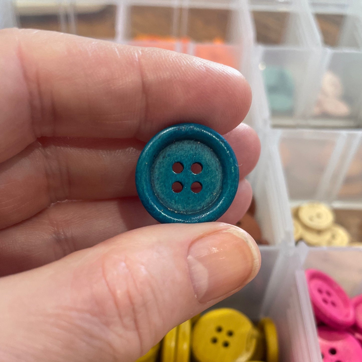 Hand holding a blue button with a container of colorful buttons in the background