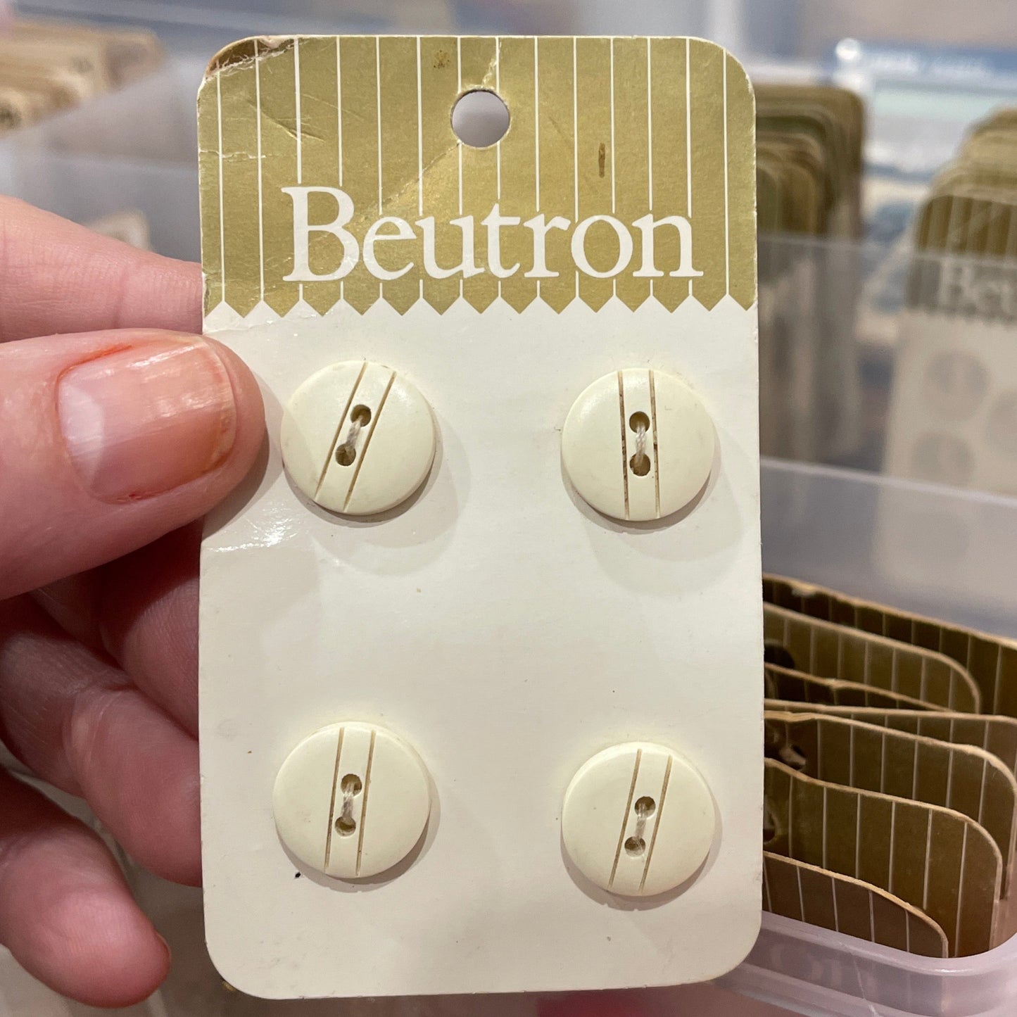 Beutron button packaging held over a plastic container with items.