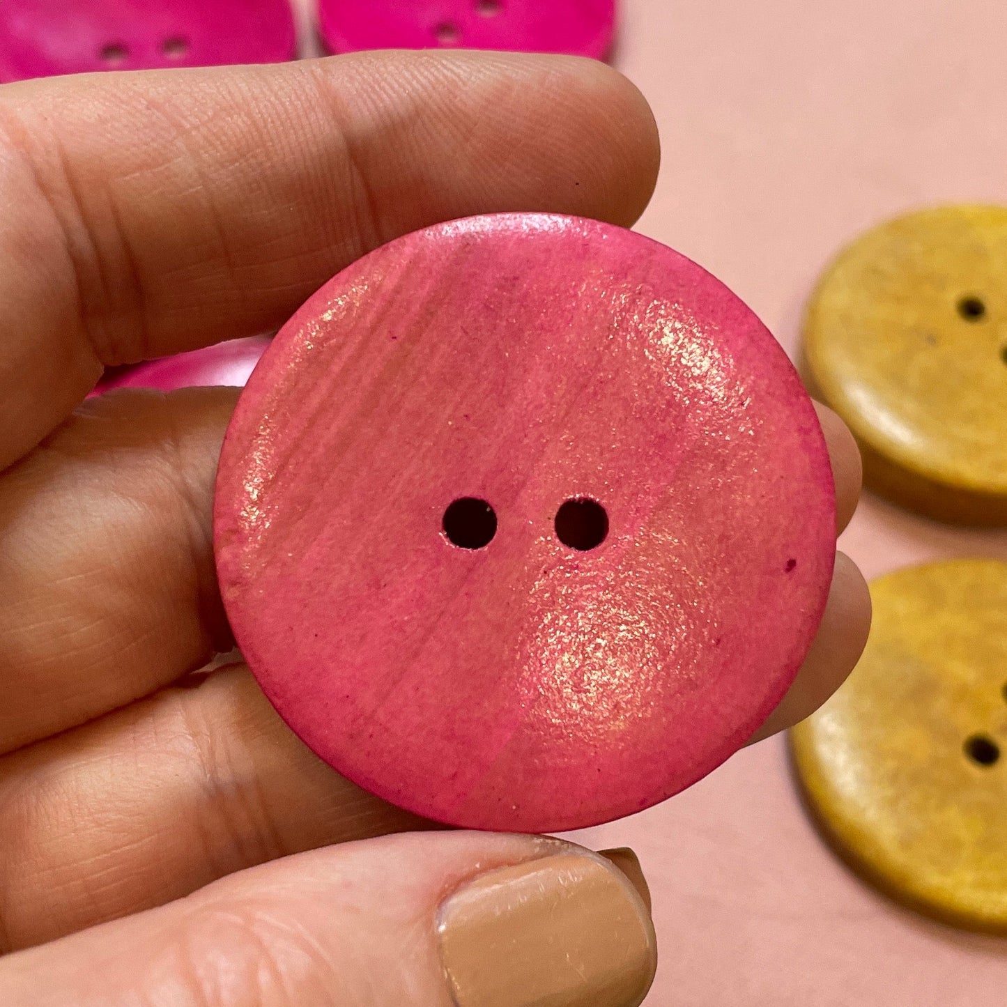 Hand holding a pink button with colorful buttons in the background
