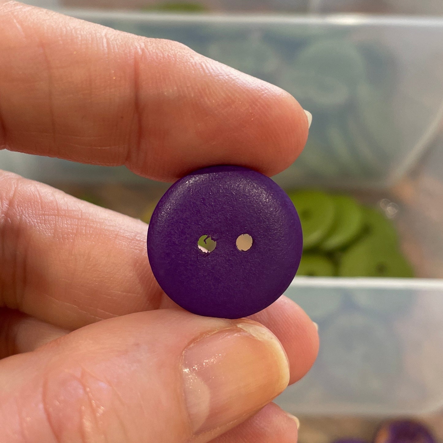 Hand holding a purple button with a clear container of buttons in the background