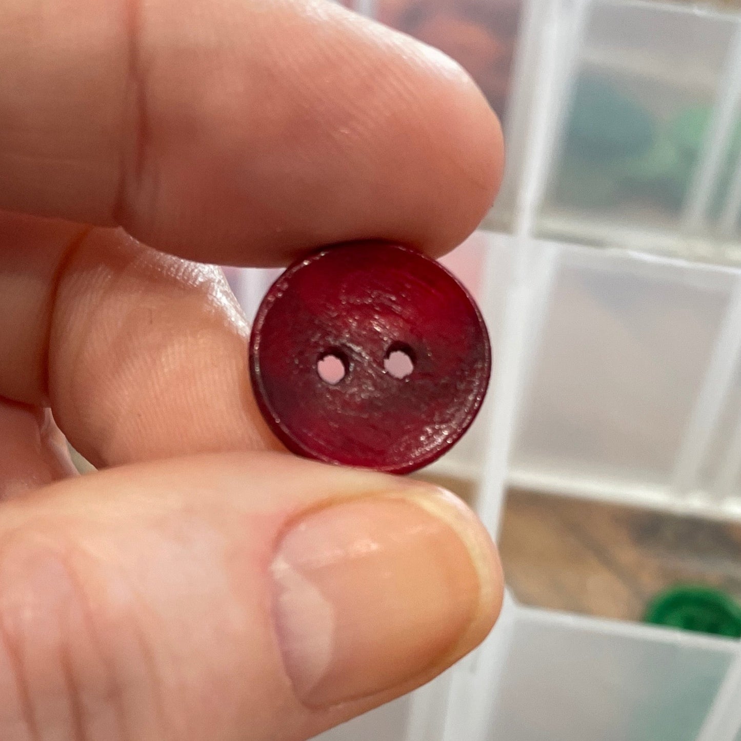 Hand holding a red button with a clear container of buttons in the background