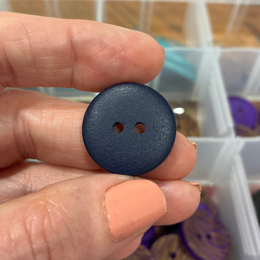 Hand holding a black button with a blurred background of a storage container with various items.